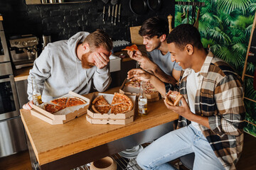 Cheerful male friends with pizza and beer talking while sitting at the table