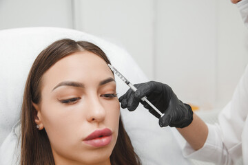 A cosmetologist makes anti-aging injections against wrinkles on the forehead on the face of a...