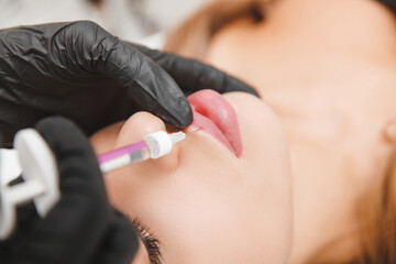 female lips, lip augmentation procedure. A syringe near a woman's mouth, injections to increase the...
