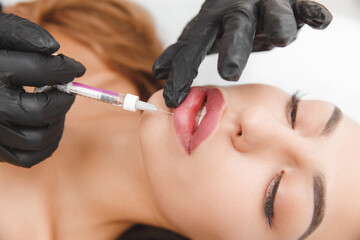 female lips, lip augmentation procedure. A syringe near a woman's mouth, injections to increase the...