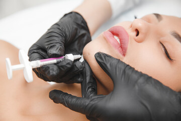 A cosmetologist makes lipolytic injections to burn fat on a woman's chin against a double chin....