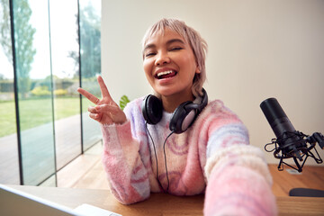 POV Shot Of Female Vlogger Holding Camera Recording Video At Home Making Peace Sign