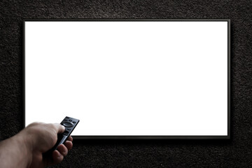 Television on a dark gray wall and remote control in hand. TV 4K flat screen lcd or oled, White...