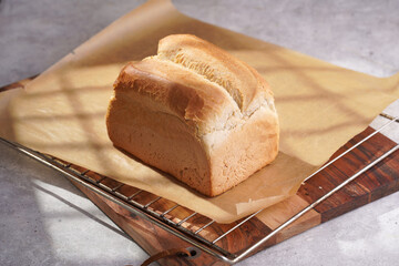 One whole freshly baked loaf of white wheat bread on baking paper on wooden board