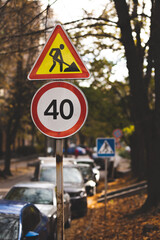 Road sign about repair work and speed limit on the background of the road and autumn trees