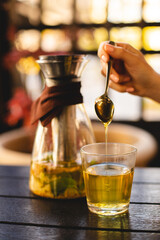 Herbal tea in a transparent teapot on bokeh background. Autumn cozy photo. Spoon of honey in a glass of tea