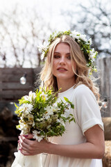 country bride in a white short dress with a wreath on her head and a bouquet of wild flowers in her hands in the village