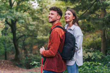 A happy couple stopped during their hike to absorb wonderful nature and breathtaking greenery. They appear to be enjoying their adventure. - obrazy, fototapety, plakaty