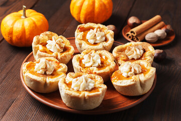 Pumpkin mini pies with whipped cream and spices on a wooden background