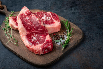 Two steak raw striploin (New York) of beef on a wooden board with seasoning, salt and red pepper....