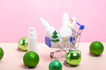 A set of skin care cosmetics in a shopping cart and Christmas tree decorations. Moisturizing face cream with Christmas accessories. Buying Christmas gifts. Winter skin care concept.