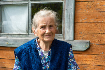 Portrait of an old peasant woman sitting near a village house.