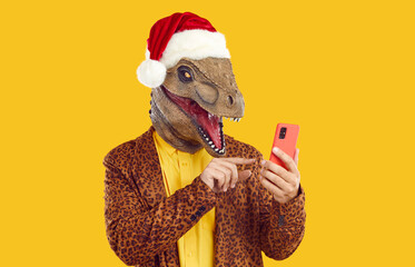 Funny excited dinosaur man in Christmas hat using mobile phone. Male fashion model wearing weird...