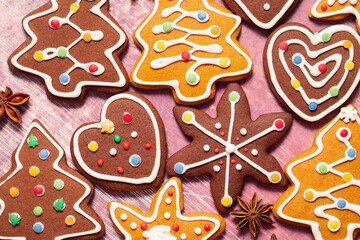 Ginger cookies in the form of Christmas trees, snowflakes, hearts are decorated with icing, confetti, anise stars on a worn pink background. Top view - 544432934