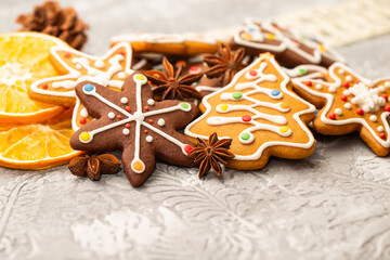 Ginger cookies in the form of Christmas trees, snowflakes, hearts decorated with icing, candy, anise stars and dried orange slices on a gray background. - 544432997