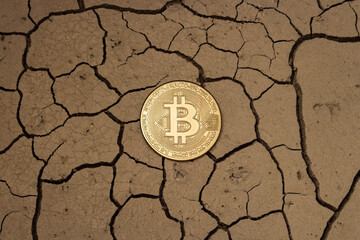 Golden bitcoin in the form of a coin lies on dry ground