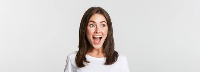 Portrait of joyful pretty brunette girl looking left amused, smiling excited and surprised over...