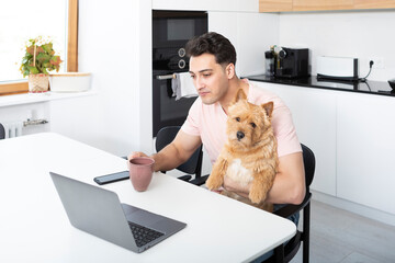 Happy handsome man hugs his pet dog Norwich Terrier and working on laptop at home