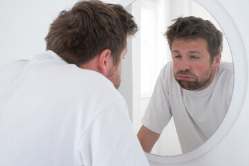 Tired mature caucasian man is looking at the mirror.