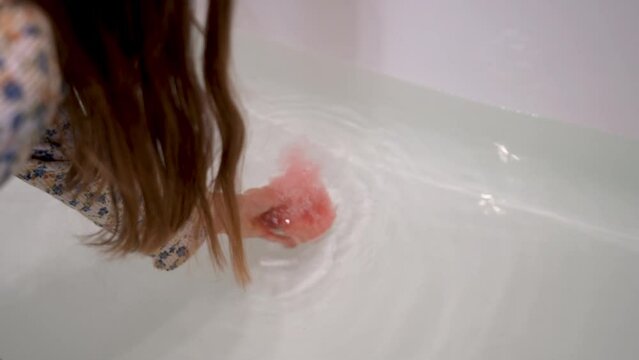 Girl lowers a foamy aromatic pink bomb into the bath. Dissolving bubbling orange bath bomb.