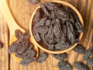 Black raisins in a wooden bowl on a textured old wood background. copy space.