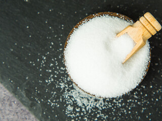 White salt on a dark concrete background in a wooden bowl and spoon