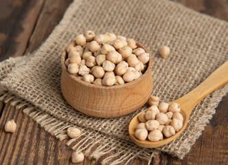 Wooden bowl and wooden spoon full of chickpeas on a wooden background.