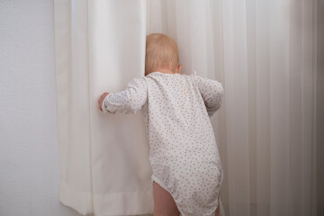 Little baby child playing with the white curtain, child have fun indoor