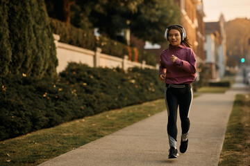Young Asian sportswoman wearing headphones while running on street.