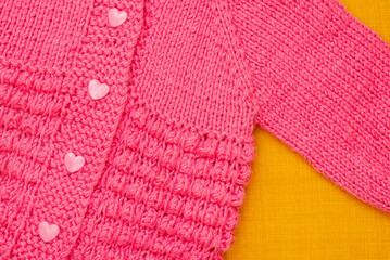 handmade children pink sweater with heart shaped buttons on a yellow background, made with love