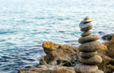 kid boy sitting on big rock seashore coast line playing with stones building pyramid.pebbles one over another zen wellbeing yoga relax meditation spa concept.water waves hit beach summer vacation