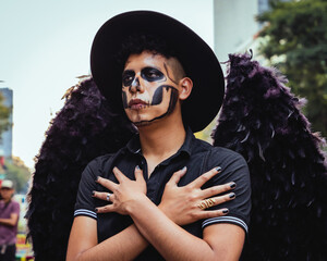 Joven caracterizado como catrín con alas de angel y sombrero negro, en el desfile de Día de...