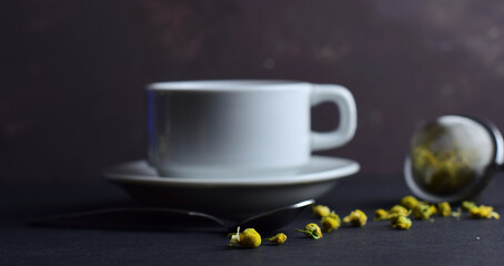 Background,
scattered chamomile, cup and filter prepared for infusion, all on a dark background.