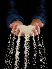 Rice grains in hands on a dark background. Hands of man pour grain of rice. Close-up