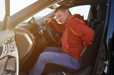 A tired driver holds on to his back, which hurts after a long drive