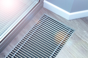 Metal grate for convector heating in the floor next to the window.