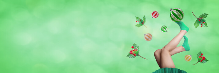 Fototapeta na wymiar Women's legs in red socks holds Christmas ball on a green Christmas background