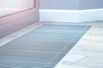 Floor convector heating metal grate built into the floor next to the window.