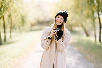 young beautiful girl is resting in nature with camera. woman photographer walking in the park on an autumn day