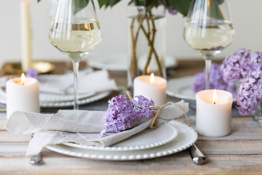 Beautiful table decor for a wedding dinner with a spring blooming lilac flowers. Celebration of a special event. Fancy white plates, wineglasses, candles. Countryside style