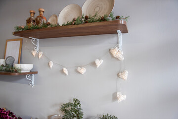 Stylish, concise Kitchen decoration for Christmas. Wooden shelves with plates, decorated with a garland and spruce branches. Fashionable minimalism in interior design