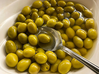 Delicious green natural fresh marinated wholesome olives with pit in a plate with tongs