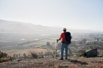 mature latin male hiker standing on the hill looking at the horizon over the valley back view