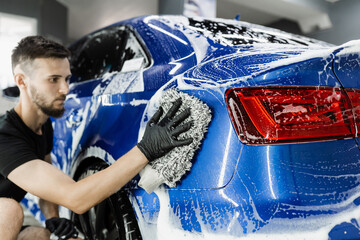 Car washer doing manual foam washing in auto detailing service. Hand washing with microfiber glove...