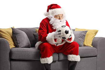 Surprised santa claus holding a football and sitting on a sofa