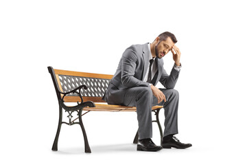 Sad businessman sitting on a bench and holding his head - obrazy, fototapety, plakaty