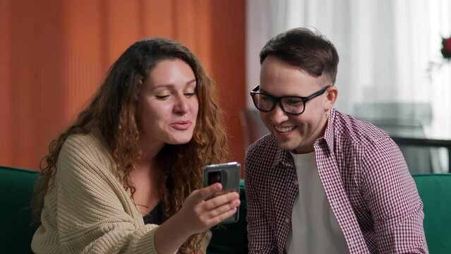 Couple discuss news on smartphone and gesture high-five sitting on couch. Man with bionic arm