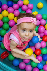 Fototapeta na wymiar Baby girl playing in colorful polka dot pool in ball bath