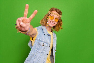 Portrait of positive cheerful hippy person hand fingers demonstrate v-sign isolated on green color background