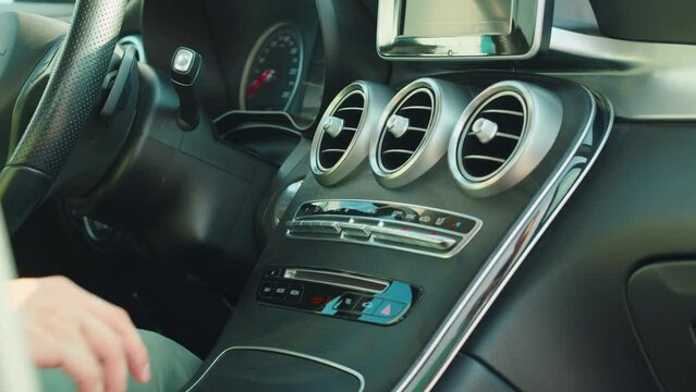 Man in luxury car, details of start stop, transmission and choosing climate control in the electric car. Man regulating temperature on car air condition. Modern car interior